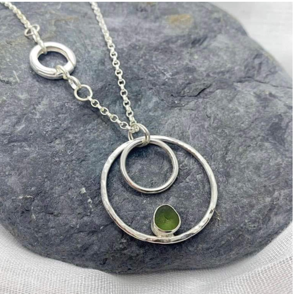 An image of a silver necklace that is comprised of 3 silver circles that get bigger in size, the smallesthas a piece of sea glasses set within the circle